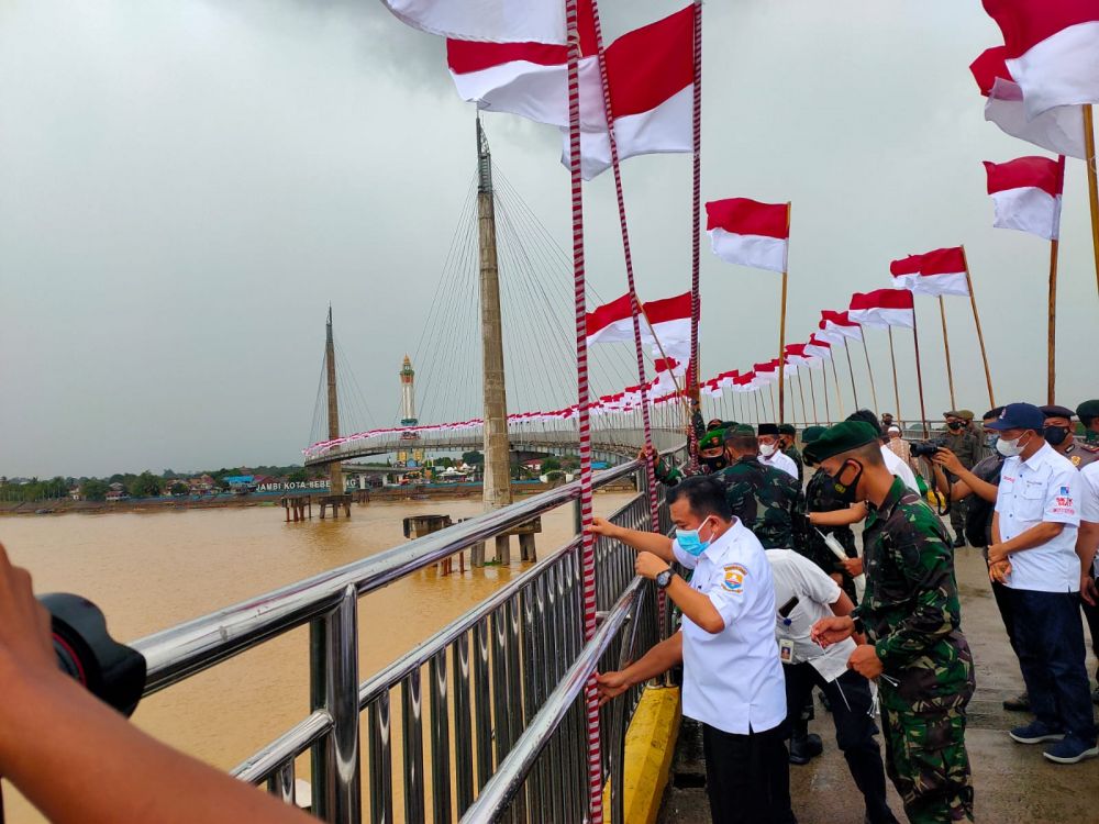 Gubernur Al Haris turun langsung memasangkan bendera merah putih di tengah jembatan pedestrian saat hujan mengguyur.